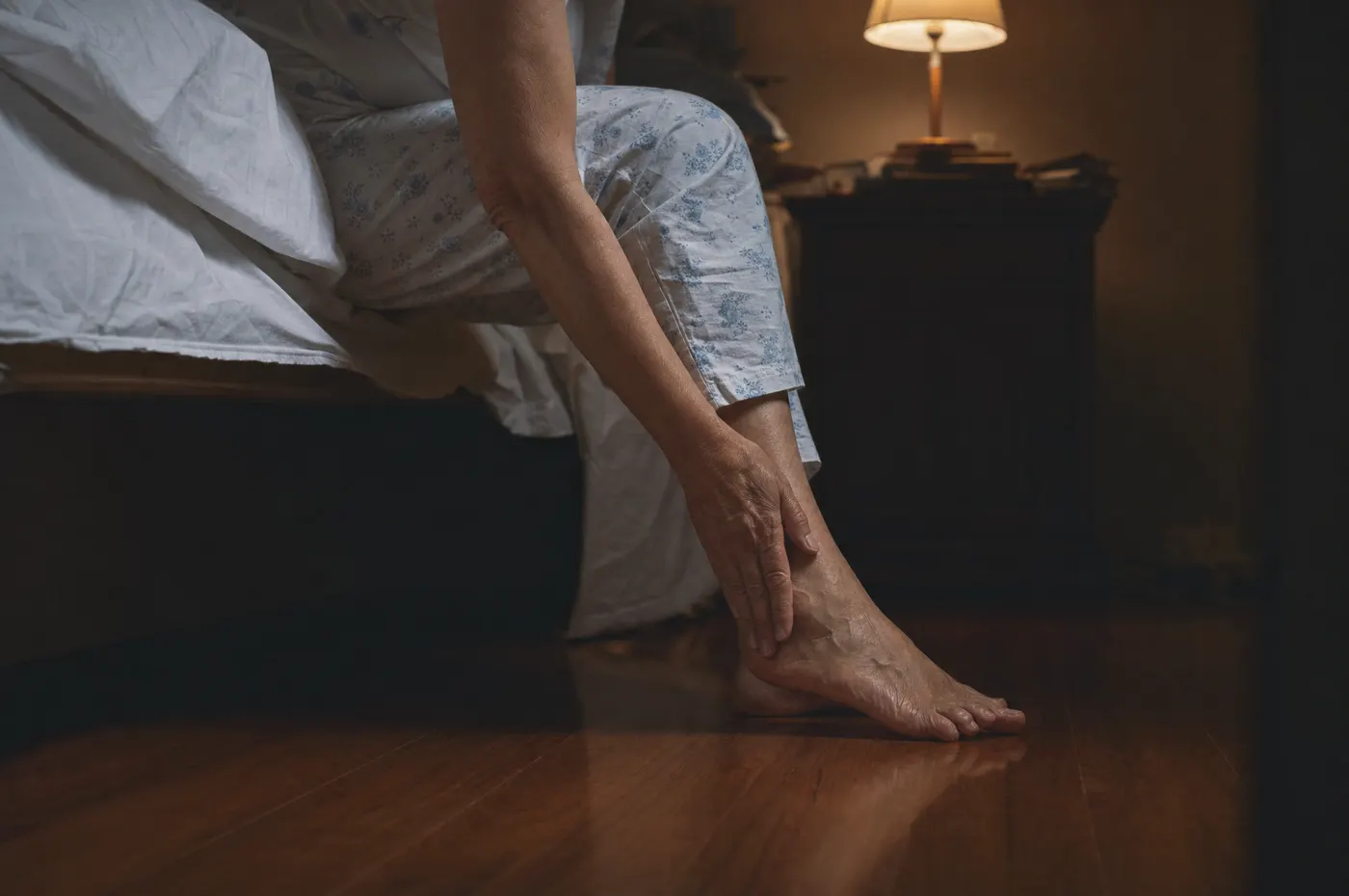 Person sitting on the edge of the bed at night, rubbing an aching foot